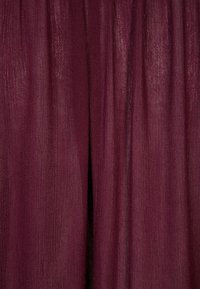 Tissu transparent bordeaux avec une texture fluide, présentant des plis verticaux et un léger éclat, créant une apparence légère et aérienne.