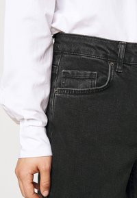 Svarta jeanstyger med smal passform, som har en bakficka med nitar, strukturerad kvalitet och midja av medelhöjd.