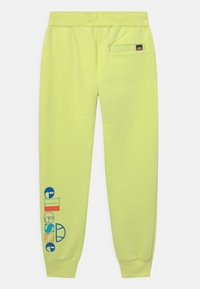 Jasnożółte spodnie dresowe z prążkowanym pasem w talii i mankietami przy kostkach. Zawierają kieszeń boczną oraz kolorowy nadruk logo "ellesse" na nogawce.