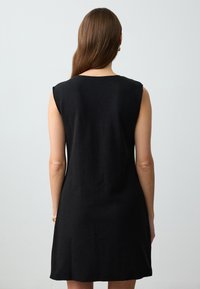 Schwarzes ärmelloses Kleid mit lockerem Schnitt und geradem Design, das eine glatte Textur und ein minimalistisches Design aufweist und bis zur Mitte des Oberschenkels reicht.