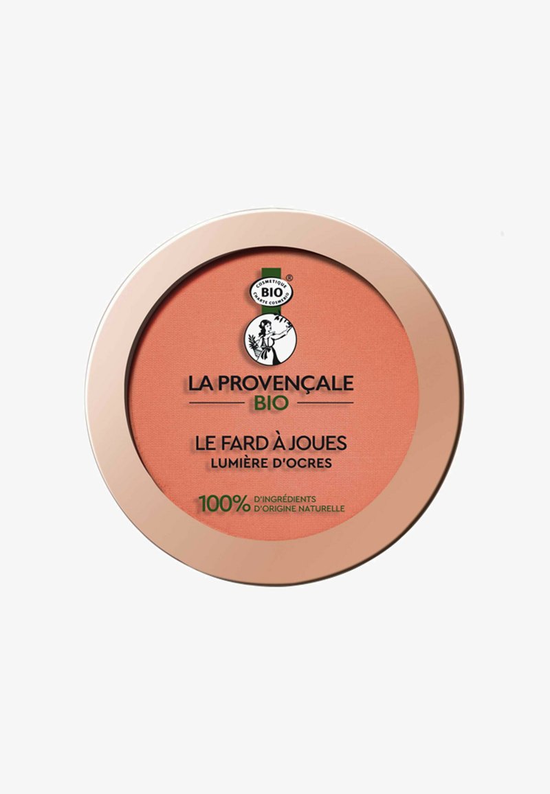 Poudrier de blush de forme ronde, présentant une teinte corail et une texture lisse. Le couvercle est bordé d'or et affiche une étiquette de produit biologique.
