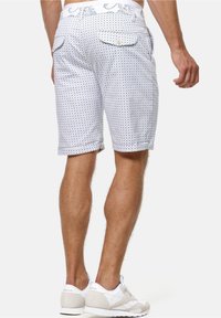 Shorts blancs avec un motif circulaire bleu, comportant deux poches arrière avec rabats. Fabriqués en tissu, ils ont une coupe décontractée et un style casual.