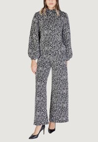 Jumpsuit con pattern bianco e nero, maniche puff lunghe e colletto alto; gamba larga e tessuto testurizzato. Abbinato a tacchi alti neri.