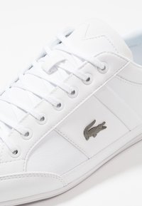 Baskets blanches avec tige en cuir lisse, semelle en caoutchouc, bout rond et logo gris. Elles sont dotées de lacets plats et d'œillets en métal.