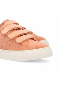 Des baskets en suède pêche présentent trois bandes Velcro ajustables, une forme arrondie à l’avant, une semelle plate en caoutchouc blanc et des détails perforés sur le côté.