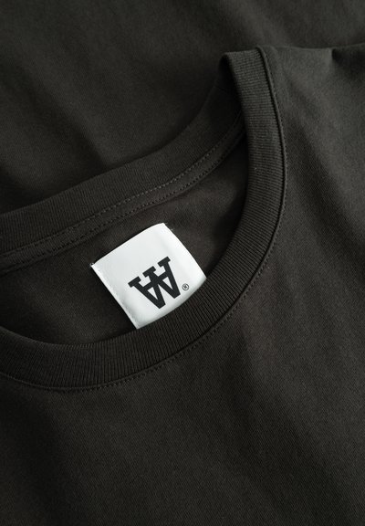 T-shirt marrone scuro con colletto a girocollo, realizzato in cotone morbido. Presenta un'etichetta bianca con testo nero all'interno del colletto. Texture liscia.
