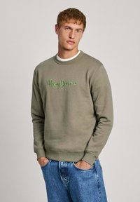 Sudadera verde oliva con cuello redondo y puños de canalé, con logo bordado de "Pepe Jeans" en verde claro. Usada sobre una camiseta blanca.