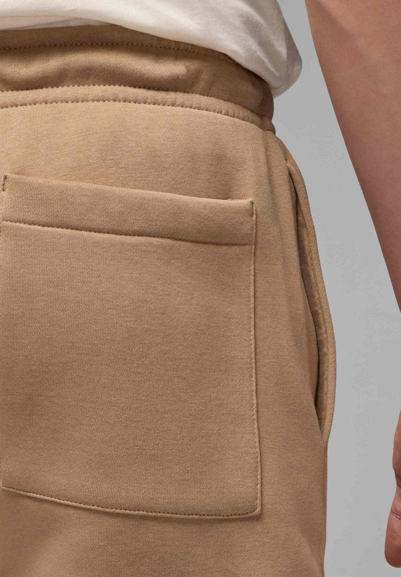 Tissu de sweat-shirt beige avec une poche latérale, présentant une couture plate et une texture douce. La taille est élastique et la silhouette est décontractée.