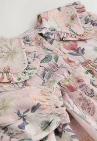 Floral-patterned dress in light pink fabric. Features ruffled collar, button closure, and gathered sleeves with subtle texture.