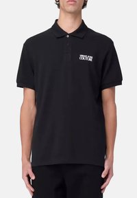 Polo shirt noir en coton, arborant un logo de marque "VERSACE JEANS COUTURE" sur le côté gauche de la poitrine, à manches courtes et avec un col classique.