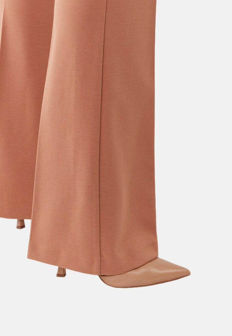 Spitz zulaufende Pumps aus weichem beige Leder, kombiniert mit weit geschnittenen Hosen aus einem pfirsichfarbenen, strukturierten Stoff, der saubere Linien und eine maßgeschneiderte Passform bietet.