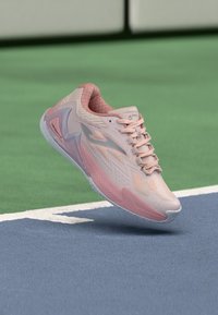 Helle rosa Sportschuh mit strukturiertem Obermaterial, kantigem Design und durchscheinender Sohle. Mit Schnürsenkeln und einem Markenlogo an der Seite.