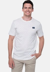 Hvid kortærmet t-shirt med et flerfarvet stjernemønster. Indeholder et lille logo-patch i marineblå på venstre bryst.