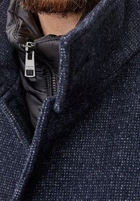 Cappotto in lana testurizzata blu navy con colletto alto, presenta un interno imbottito nero e una cerniera argentata con dettaglio del marchio.