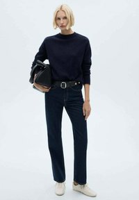 Pulover tricotat bleumarin, blugi negri cu talie înaltă, centură neagră cu cataramă argintie, geantă neagră, adidași albi; ținută casual minimalistă.