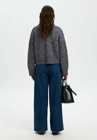 Skrócony, dzianinowy sweter w ciemnofioletowym kolorze z teksturowanym wzorem, w połączeniu z szerokimi niebieskimi dżinsami i małą czarną torebką z detalem w kształcie kokardy.