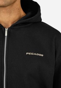 Juodas užtrauktukas gobtuvas, pagamintas iš medvilnės mišinio, su pilku "PEGADOR" logotipu ant krūtinės ir tekstūruoto audinio apdaila.