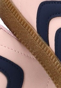 Zapatilla de color rosa claro con acentos en azul marino oscuro, suela de goma texturizada y detalles con costuras. Diseño elegante y forma redondeada.