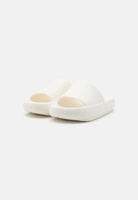 White slip-on sandals with a textured upper and open toe design. Thick sole, smooth finish, minimalistic style. Suitable for casual use.