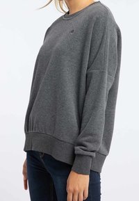 Grijze crewneck sweatshirt van zacht materiaal met een relaxte pasvorm, voorzien van geribde mouwen en zoom, en een klein logo op de borst.