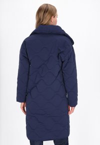 Marineblå quiltet jakke med høj krave, lange ærmer og bølget mønsterstruktur. Bagsiden har et mellemlangt design og ingen synlig udstyr.