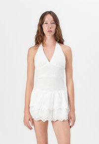 Bijela halter-neck haljina s naboranim korzetom i višeslojnim, valovitim rubom. Sadrži eyelet detalje na slojevima, lagani materijal.