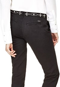 Jean noir au design ajusté, avec une taille cloutée, des détails sur les poches arrière et une texture en coton lisse.