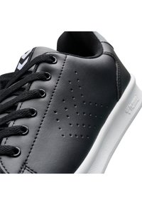 Baskets en cuir synthétique noir avec lacets noirs, perforations circulaires sur le côté et semelle en caoutchouc blanche. Logo simple sur le talon.