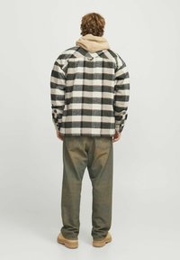 Giacca a quadri nera, bianca e grigia con una vestibilità ampia; felpa beige sotto, abbinata a jeans verdi larghi e stivali color sabbia.