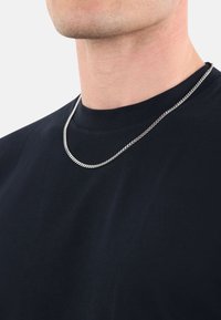 Una collana in argento si poggia su una maglietta nera a girocollo, caratterizzata da una texture liscia e un classico design a maglie piatte.