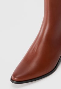 Brune lær ankle boot med en slank spiss tå, blank finish og en kontrastfylt svart såle. Glatt tekstur med minimale detaljer.