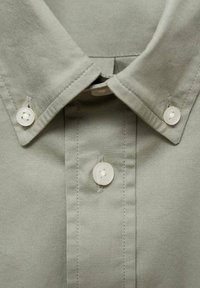 Lichtgrijs button-up shirt met een puntige kraag, een centrale sluiting met drie ronde, witte knopen en een gladde textuur.