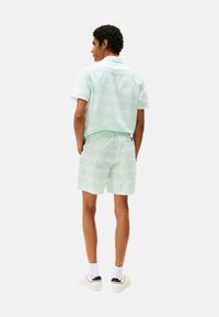 Camicetta verde menta a maniche corte e pantaloni abbinati con un motivo sottile. Il modello indossa scarpe bianche e calzini bianchi ben visibili.