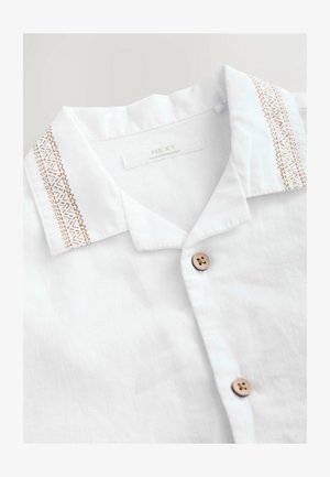 Vit skjorta med krage och texturerad broderad detalj i ljusbrunt, försedda med två runda träknappar framtill.