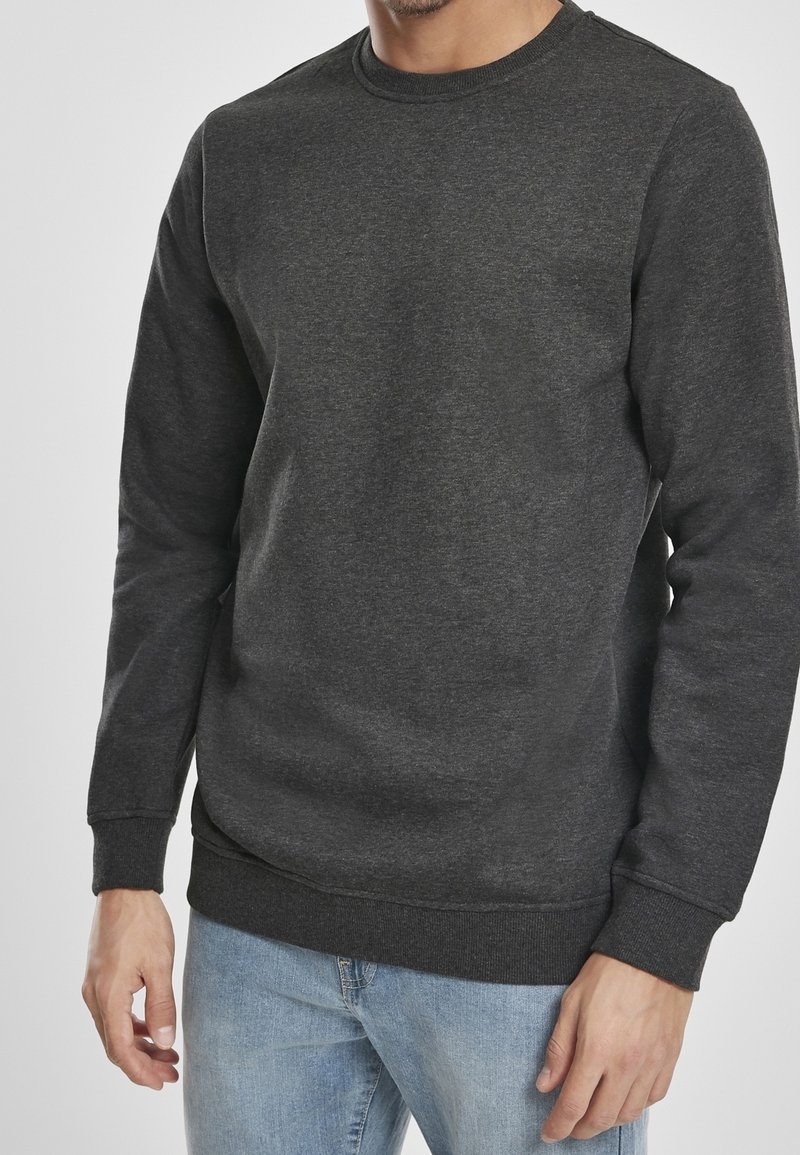 Sweat-shirt gris foncé à col ras du cou avec poignets et ourlet côtelés, fabriqué dans un tissu doux et texturé. Porté avec un jean en denim bleu clair.