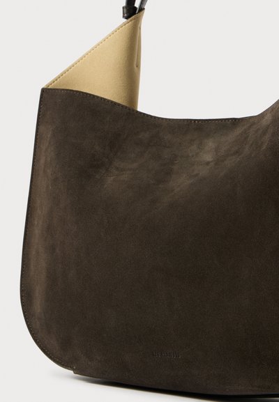 Borsa hobo in suede marrone scuro con una texture liscia, grande forma tondeggiante e interno beige a contrasto. Presenta un design minimalista.