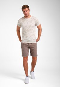 T-shirt beige à manches courtes avec un motif de feuilles, associé à un short marron clair et des baskets blanches. Tissu doux et coupe décontractée.