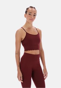 Bordowy krótki top na ramiączkach z falbanowym końcem, połączony z legginsami o wysokim stanie w tym samym kolorze i gładkiej fakturze.