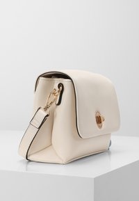 Borsa a mano in pelle crema con un design strutturato, hardware dorato e chiusura a patta. Tracolla regolabile e dettagli in contrasto neri.