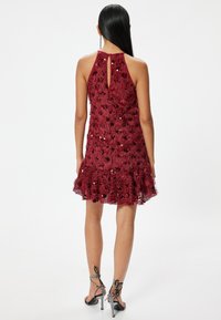 Robe sans manches bordeaux avec un ourlet évasé, en tissu texturé et ornée de sequins. Détail en forme de clé à l'arrière qui accentue le design.