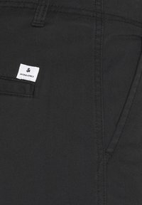 Nahaufnahme einer schwarzen Stoffhosentasche mit sichtbaren Nähten und einem kleinen weißen Textillabel mit der Aufschrift Jack & Jones.