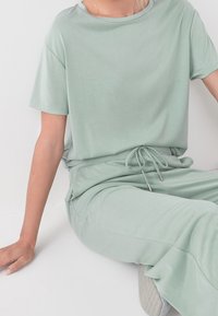 Lichtgroene loungewearset met een ontspannen pasvorm, korte mouwen top en elastische taillebroek met strik en zilverkleurige accenten.