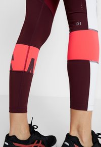 Viininpunaiset ja vaaleanpunaiset leggingsit väriblokeilla ja logolla; joustavasta materiaalista, korkealla vyötäröllä ja nilkkapituudella.
