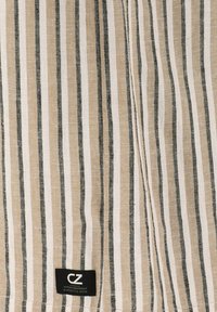 Beige och vit randig tyg med svarta accenter. Har en texturerad väv och en svart etikett med vit text längst ner.