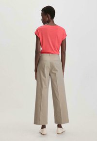 Licht koraalkleurig shirt met korte mouwen gecombineerd met licht beige wijde broek. De broek heeft voorplooien en achterzakken.