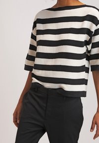 Czarny i biały pasiasty krótki top z szerokim dekoltem typu łódka, zestawiony z czarnymi spodniami. Dzianinowa faktura i luźny krój.