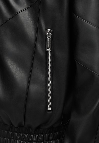 Fekete bőrdzseki, hangsúlyos ezüst cipzárral és gumírozott derékrésszel. Sima textúra, átlós varrási mintázattal.