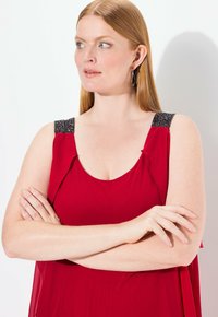 Vestido rojo sin mangas con detalles de volantes y tirantes de hombro con cuentas. Tejido suave y diseño fluido, acentuando el escote.