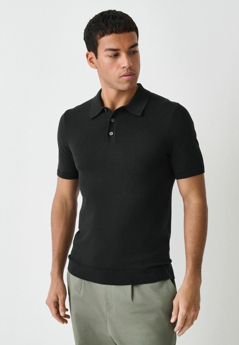 Polo de manga corta negro en material de punto suave con tres botones y cuello, que presenta un diseño ajustado y dobladillo acanalado.