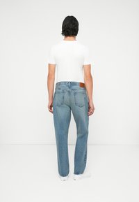 Jeans de denim ligeros y holgados de color azul claro con una parche de cuero marrón en la parte trasera y bolsillos traseros visibles, combinados con una camiseta blanca sencilla.